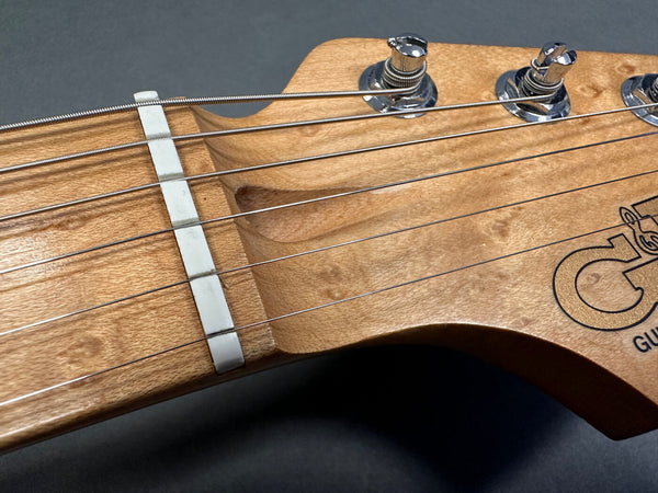 Close-up of Coffee House Guitars wooden guitar headstock with metal tuning pegs and strings on dark background