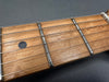 Close-up of maple guitar fretboard with metal frets and steel strings on dark background