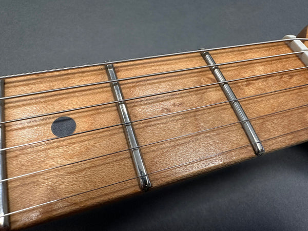 Close-up of maple guitar fretboard with metal frets and steel strings on dark background