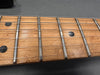 Close-up of guitar fretboard with metal frets, black dot inlays, and steel strings on natural wood finish neck
