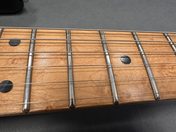Close-up of guitar fretboard with metal frets, black dot inlays, and steel strings on natural wood finish neck