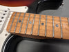Close-up of maple fretboard with dot inlays and metal frets on electric guitar with sunburst body and white pickguard