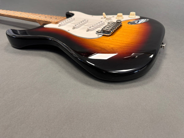 Electric guitar with sunburst finish, white pickguard, and maple neck on gray surface, close-up detail of body and bridge.