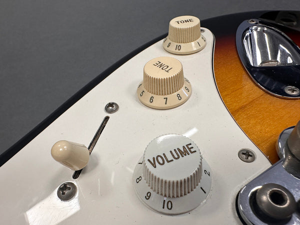 Close-up of electric guitar tone and volume control knobs with white pickguard and sunburst finish body background at Coffee House Guitars