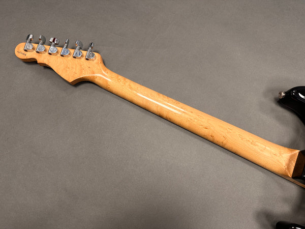 Maple guitar neck with chrome tuning pegs on electric guitar showing back headstock and part of black guitar body on grey background