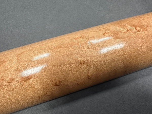 Close-up of guitar neck made from polished birdseye maple wood showing detailed grain texture on gray background