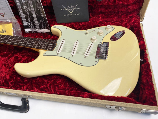 Vintage Fender Stratocaster electric guitar in ivory finish with rosewood fretboard, displayed in a red plush-lined hard case with Fender owner's manual and custom care booklet.