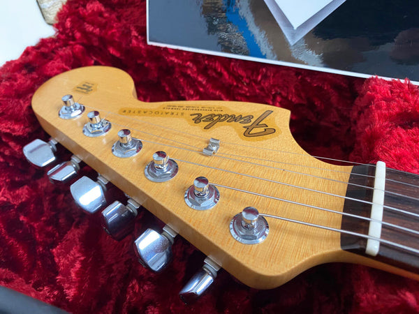 Close-up of Fender Stratocaster maple headstock with chrome tuning pegs and guitar strings in red velvet-lined case