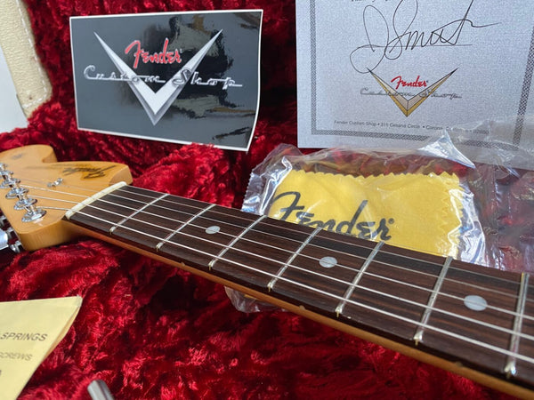 Close-up of Fender Custom Shop guitar neck and headstock on red plush case interior with Fender Custom Shop certificate and cleaning cloth in background