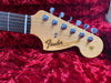 Fender Stratocaster guitar headstock with six tuning pegs on red plush case interior.