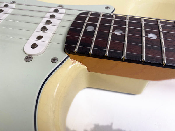 Close-up of vintage electric guitar neck joint with visible paint chip and aged cream finish, rosewood fretboard, and single-coil pickups