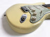 Close-up of cream-colored electric guitar body showing volume and tone knobs, input jack, and tremolo bridge on white background