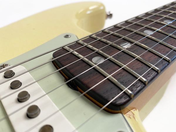 Close-up of electric guitar strings, rosewood fretboard, and single-coil pickups on cream-colored body
