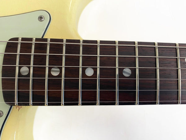 Close-up of vintage electric guitar rosewood fretboard with metal frets and dot inlays on cream-colored body