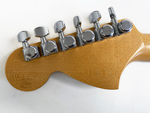Close-up of natural wood guitar headstock with six chrome tuning pegs on white background