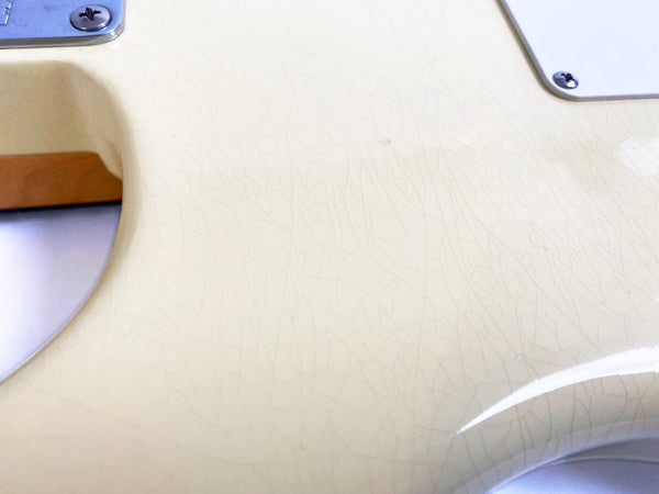 Close-up of cream-colored guitar body with vintage crackle finish and white pickguard screws visible