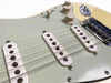 Close-up of vintage electric guitar pickups, volume and tone control knobs, and steel bridge on cream-colored body.