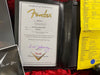 Certificate of Authenticity for Fender Custom Shop 65 Stratocaster Relic guitar dated 08/2/2019 with serial number R100353 and detailed specifications sheet on yellow paper beside it in guitar case
