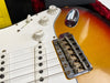 Close-up of sunburst electric guitar bridge, white pickup covers, and tone and volume control knobs with "Volume" and "Tone" labels on pickguard surface