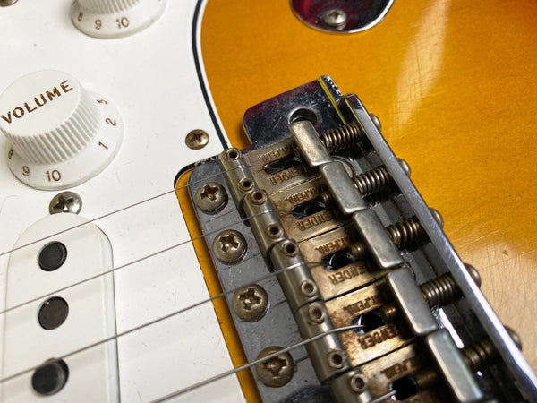 Close-up of vintage Fender electric guitar bridge and volume knob on sunburst body with white pickguard and single coil pickups