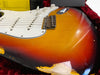 Close-up of sunburst electric guitar body with white pickguard and volume knobs, showing wear and paint chipping near the edges in a red velvet-lined guitar case