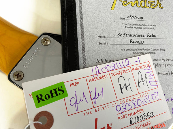 Fender 65 Stratocaster Relic guitar neck plate with serial number R100353, Fender certificate of authenticity dated 08/2/2019, and assembly inspection tag with RoHS label and part number R100353.