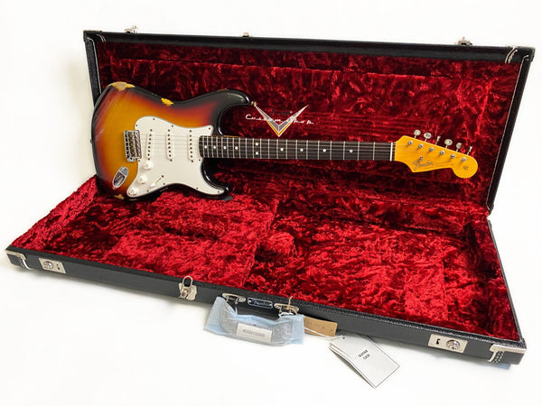 Vintage Fender Stratocaster electric guitar with sunburst finish and white pickguard in black hard case lined with red velvet interior