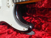 Close-up of black electric guitar body with white pickguard on red plush guitar case interior