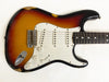 Vintage sunburst electric guitar with white pickguard and three single-coil pickups, showing wear and paint chipping on body edges, displayed on white background