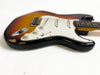 Vintage sunburst electric guitar with white pickguard and three single-coil pickups, showing wear and paint chips on body edges, displayed on white background.