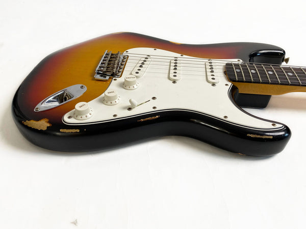 Vintage sunburst electric guitar with white pickguard and three single-coil pickups, showing wear and paint chips on body edges, displayed on white background.
