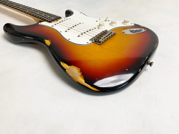 Close-up of a vintage sunburst electric guitar with worn and chipped finish, white pickguard, three single-coil pickups, and volume and tone control knobs on a white background