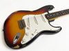 Vintage sunburst electric guitar with single-coil pickups and white pickguard showing wear and finish checking on body edges.