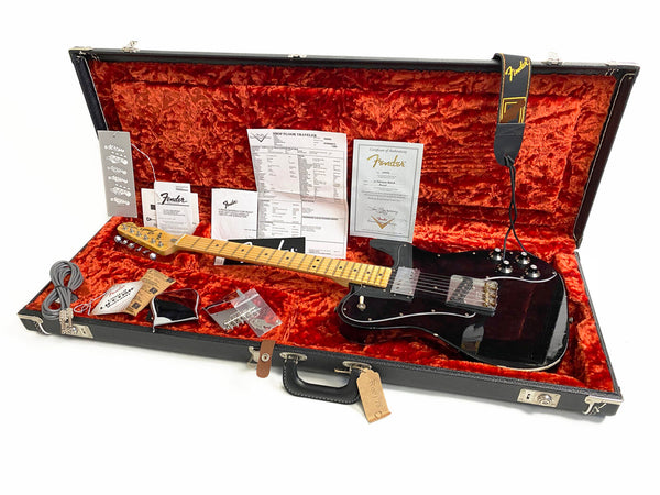 Fender black electric guitar with maple neck and fretboard in open hard case with vintage orange plush interior, Fender certificate of authenticity, extra parts, cables, and Fender strap.