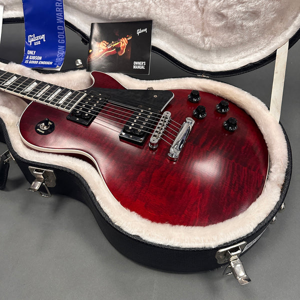 Gibson electric guitar in vintage cherry finish with black pickguard inside black hardshell case with plush lining, Gibson owner's manual and warranty card visible