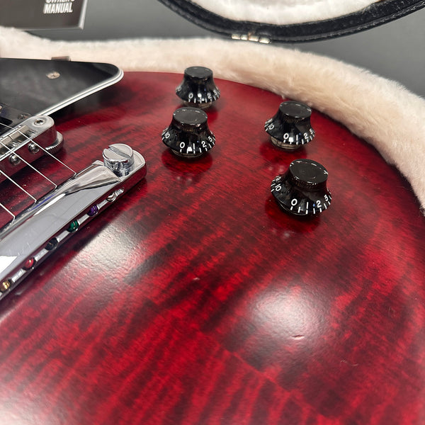Close-up of red electric guitar body with black control knobs and chrome bridge in plush case