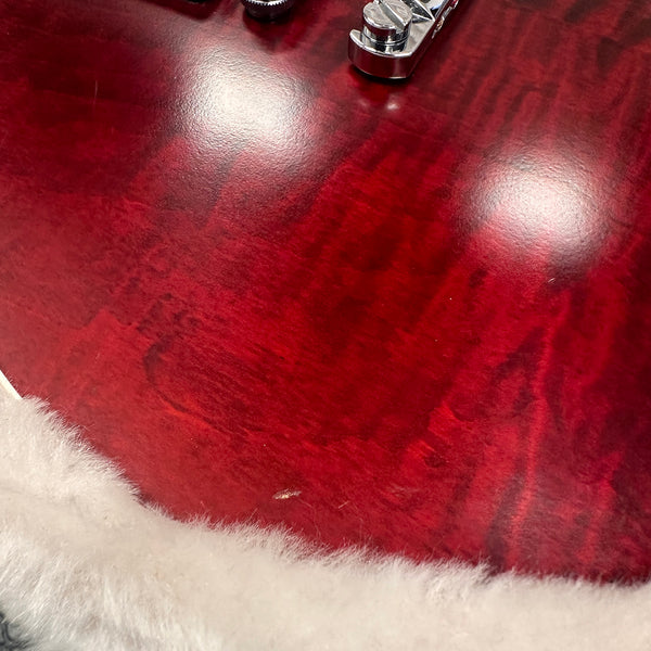 Close-up of a red quilted maple guitar body with chrome hardware and white plush lining in a guitar case