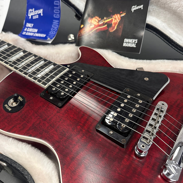 Close-up of red Gibson electric guitar with dual humbucker pickups and rhythm toggle switch in plush lined guitar case with Gibson owner's manual and tag