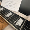 Close-up of guitar fretboard with pearl block inlays and metal strings inside a plush-lined guitar case with inspection and packing certificate