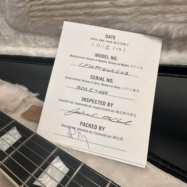 Guitar inspection certificate with model number and serial number inside plush guitar case next to guitar neck with mother of pearl inlays.
