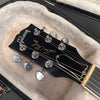 Close-up of Gibson Les Paul guitar headstock with tuning pegs and strings inside a plush-lined black guitar case