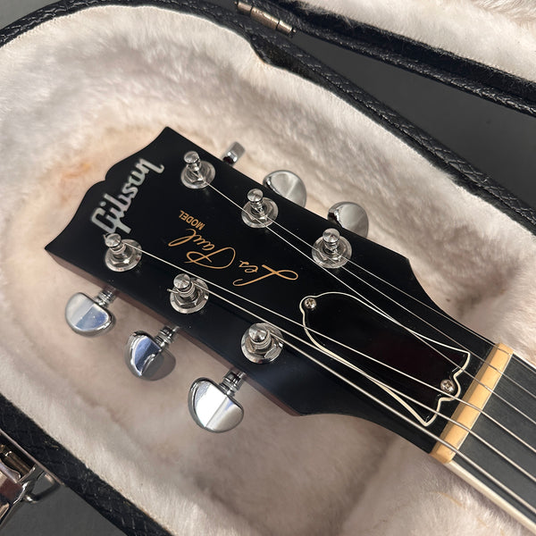 Close-up of Gibson Les Paul guitar headstock with tuning pegs and strings inside a plush-lined black guitar case