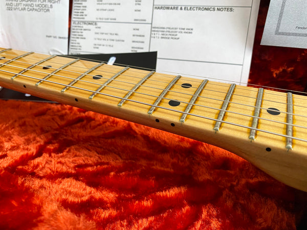 Close-up of maple guitar neck and fretboard with dot inlays and steel strings on red plush guitar case lining and documentation in background