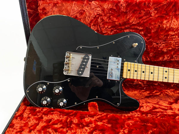 Black electric guitar with maple neck and fretboard, chrome pickups, and four black control knobs, resting on vintage red plush guitar case interior