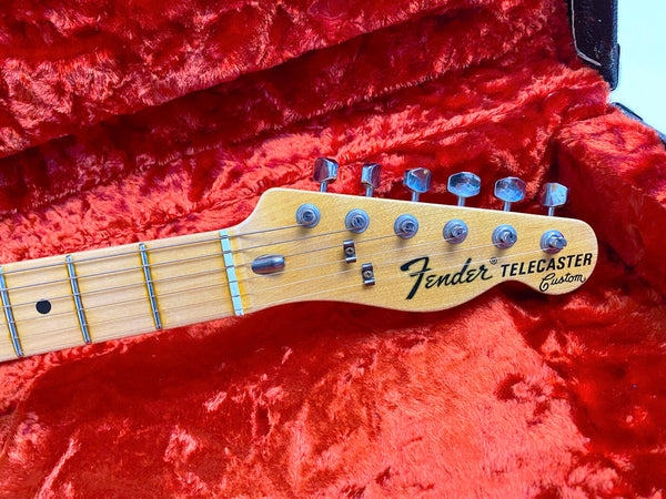 Close-up of Fender Telecaster Custom electric guitar headstock and tuning pegs on red plush guitar case interior