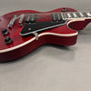 Close-up of cherry red electric guitar body with dual humbucker pickups, black pickguard, chrome bridge, and control knobs on grey background.