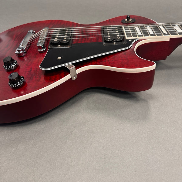 Close-up of cherry red electric guitar body with dual humbucker pickups, black pickguard, chrome bridge, and control knobs on grey background.