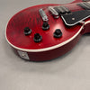 Close-up of red electric guitar body with black control knobs, chrome bridge, and pickup pickups on gray background