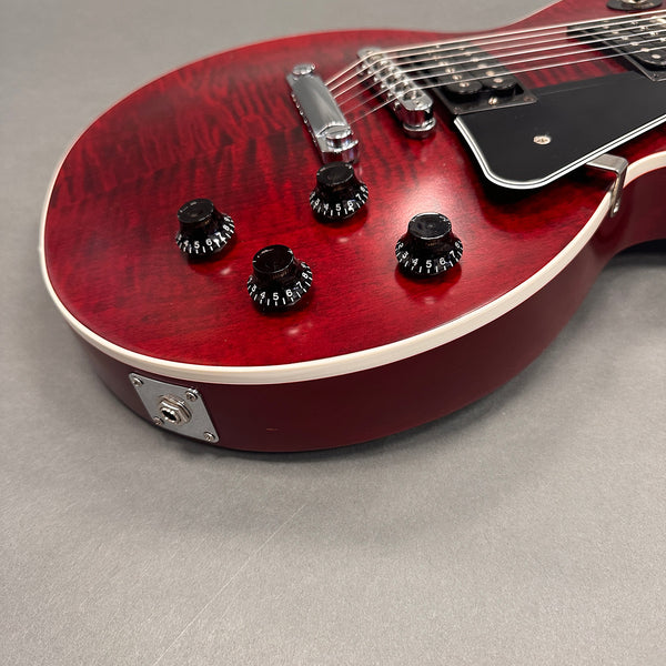 Close-up of red electric guitar body with black control knobs, chrome bridge, and pickup pickups on gray background