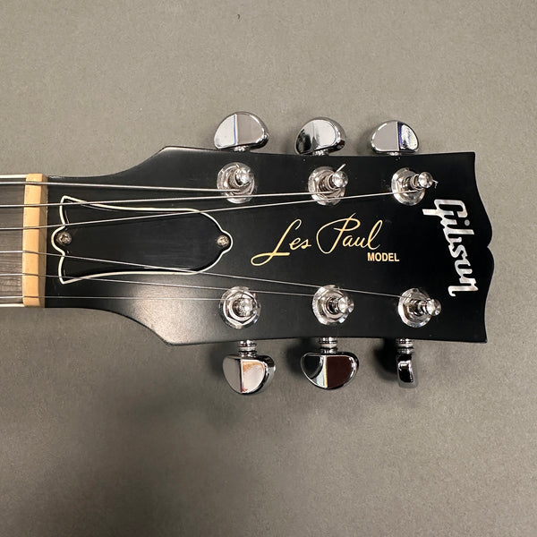 Close-up of black Gibson Les Paul Model guitar headstock with chrome tuning pegs and white logo on gray background
